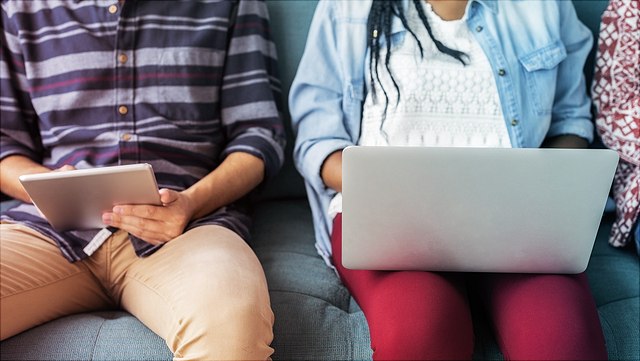 Menschen auf Sofa Ein Mädchen mit Laptop und ein Junge mit Tablet auf einem Sofa