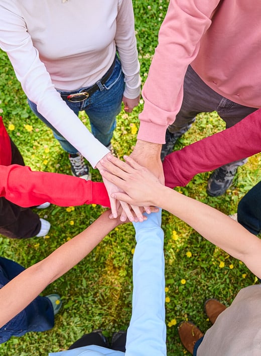 7 Personen, die die Hände in der Mitte zusammenlegen